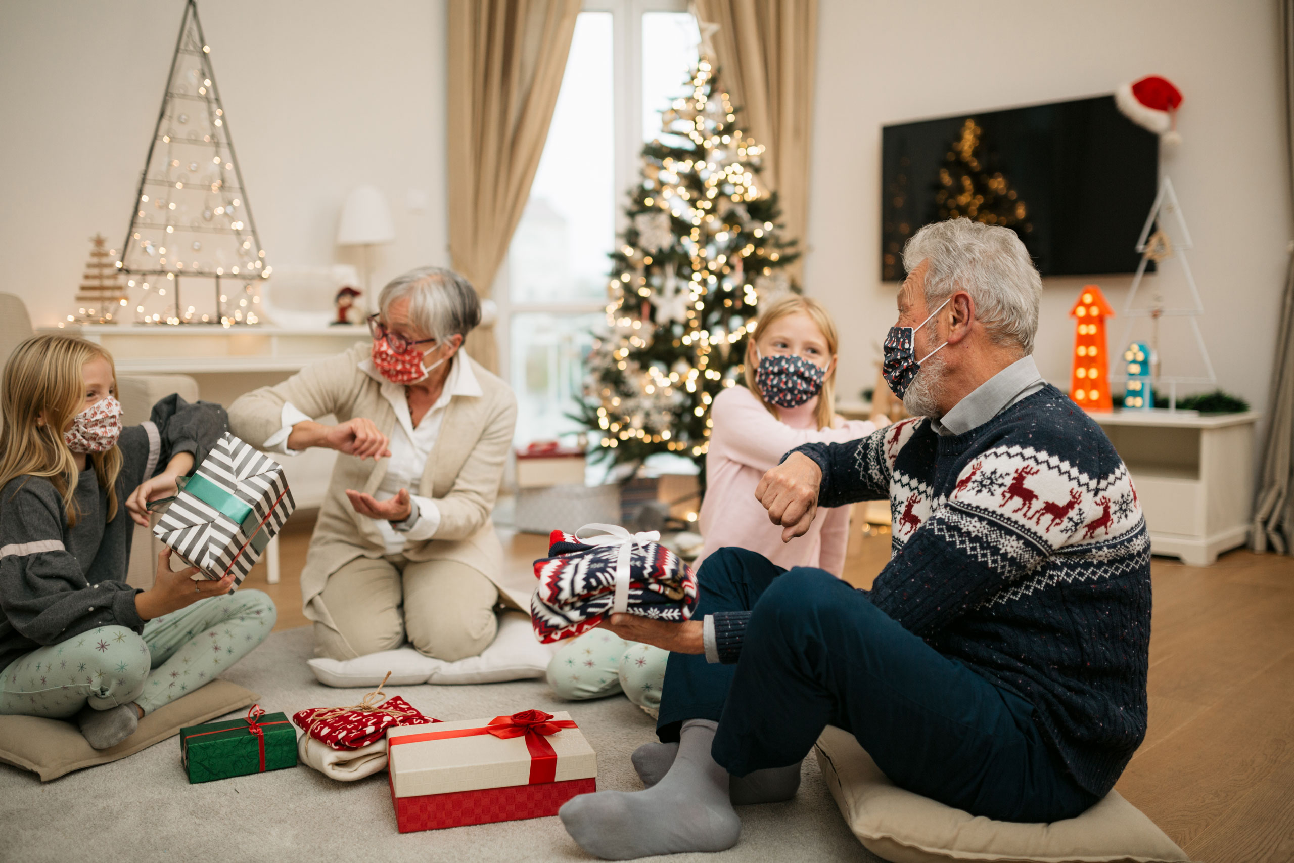 Two twin girls opening gifts with their grandparents at home for Christmas, wearing a protective face mask and maintaining social distancing